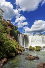 Impressive waterfall with neighbouring building and flag, blue sky and lush greenery, The Iguazu
