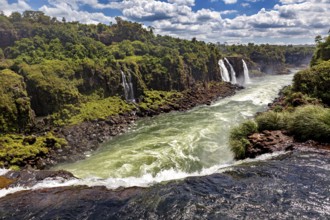 A wide river crosses a rocky gorge surrounded by green vegetation, The Iguazu Falls between