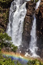 Large waterfall surrounded by rocks with a rainbow nearby, surrounded by forest, The Iguazu Falls