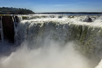 A mighty waterfall with rising spray under a clear blue sky, The Iguazu Falls between Argentina and