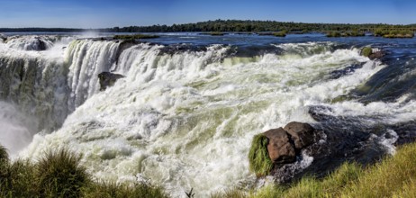 Panoramic view of the raging river and waterfall, surrounded by rocks and lush greenery, The Iguazu