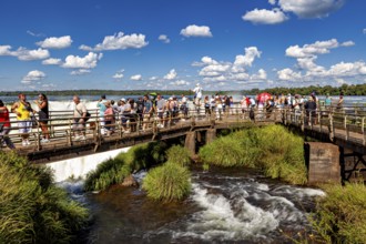 Group of tourists on a wooden bridge over a river with blue sky and clouds, tourist jetty at the
