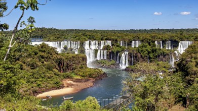 Picturesque waterfalls with a small beach on the left under a clear sky, The Iguazu Falls between