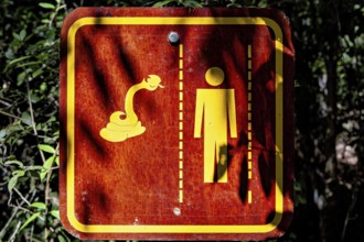 Warning sign in the forest with symbols of a snake and a human figure, An Orion Cecropian butterfly