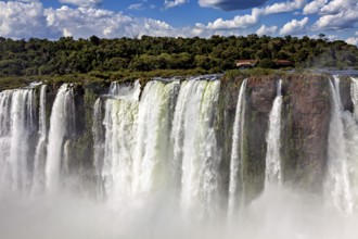 High waterfalls with rocks, spray and forested background under changing skies, The Iguazu Falls