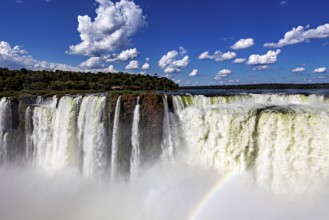 Majestic waterfall with rainbow under a clear sky and scattered clouds, The Iguazu Falls between