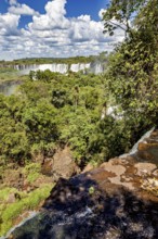 Cliff overlooking impressive waterfalls and thick vegetation against a cloudy sky, The Iguazu Falls