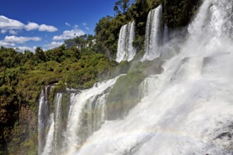 Waterfalls with dense fall and rainbow, embedded in lush forest under a blue sky, The waterfalls of