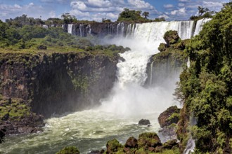 Large waterfall with dense spray and surrounding green forests under a blue sky, The Iguazu Falls