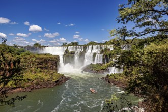 Waterfalls with boat in the river and surrounding jungle under a blue sky, The Iguazu Falls between