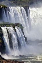 Spectacular waterfall with observation bridge, surrounded by dense vegetation and foaming spray,