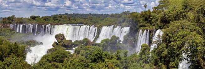 Long waterfall with lush vegetation under a sunny, cloudy sky, The Iguazu Falls between Argentina