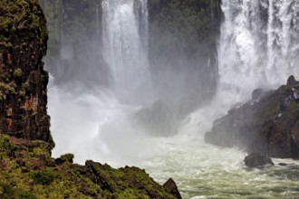 Dramatic waterfall with powerful spray, surrounded by lush vegetation and rocks, The Iguazu Falls