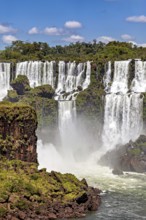 Impressive waterfalls cascade powerfully over rocks, surrounded by green vegetation and under a