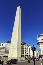 A tall obelisk under a clear blue sky surrounded by modern buildings, The Great Obelisk in the city