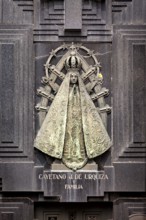 Metal relief of a Madonna on a dark stone surface with engravings and religious symbols, La