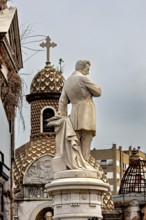 Marble sculpture in front of a decorative dome with a cross in an urban setting, La Recoleta