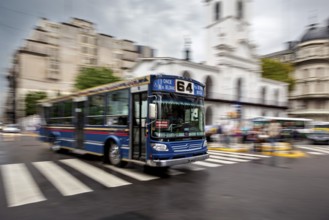 A blurred bus in motion on a city street in front of a church, The bus line 64 in the city of