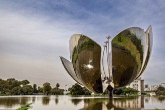 Large metal flower sculpture on the edge of a lake with a cloudy sky in the background, The lotus