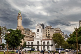 A park with a central colonial building and historic clock towers under a cloudy sky, Historic
