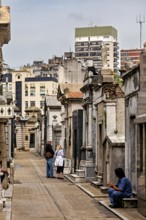 Urban cemetery alley with people and historic graves surrounded by modern architecture, La Recoleta