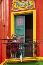 A humorous sculpture of a woman on a balcony in front of a colourful building, The colourful city