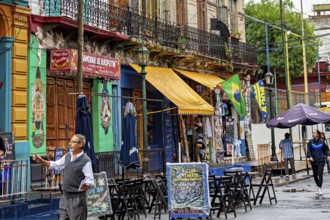 A lively street market with colourful banners and cafés, people stroll past, The colourful city and