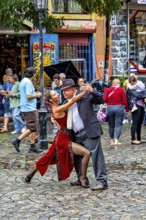 A couple performs impressive tango poses on a rain-soaked street with spectators, The colourful