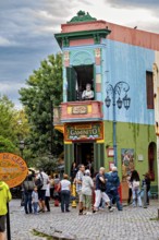 A lively place with colourful buildings and people, a statue stands on the balcony, The colourful