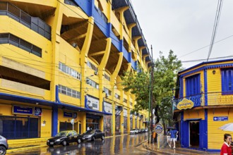 Yellow and blue stadium on a rainy street with trees and buildings, The football stadium of La