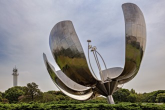 Metal flower sculpture next to a tower with a cloudy sky and green surroundings, The lotus blossom