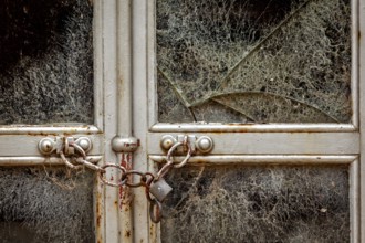 Abandoned building with a locked, rusty chain and broken window, exuding a dilapidated atmosphere,
