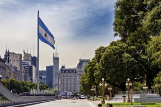 A large flag flies in front of an urban landscape with historic buildings and trees, The city of