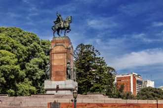 An equestrian monument on a pedestal surrounded by trees and buildings under a blue sky, The city