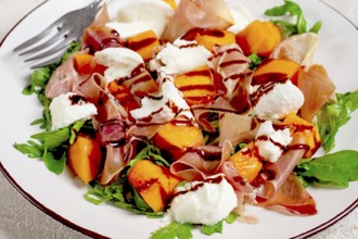 Salad with slices of ripe melon, prosciutto, mozzarella and fresh arugula, decorated with balsamic
