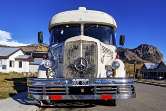 Front view of a vintage bus with Mercedes-Benz logo, against a mountainous backdrop and clear sky,