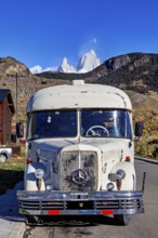 A vintage bus in front of a snow-covered mountain landscape, taken from the front view on a road, A