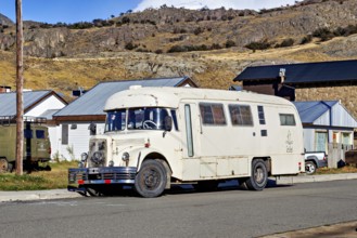 A vintage camper van parked in a mountainous landscape, surrounded by houses and clear skies, A