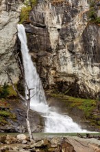 A waterfall cascades over rocky cliffs into a forest, surrounded by rocks and vegetation, waterfall