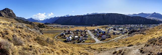 Panoramic view of a village in the valley, surrounded by high mountains and dry grassland under a