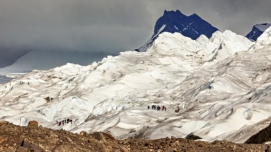 A group of people hiking on a glacier, surrounded by a harsh, icy landscape and dark mountains in