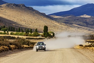 A car drives on a dusty gravel road through a mountainous landscape, Over gravel tracks through