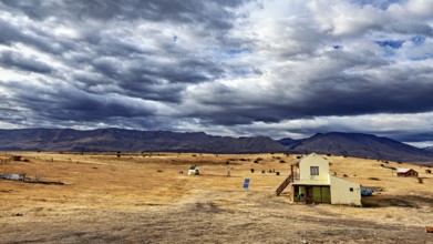 A small house in an open, rural landscape under a dramatically cloudy sky, The Patagonian landscape