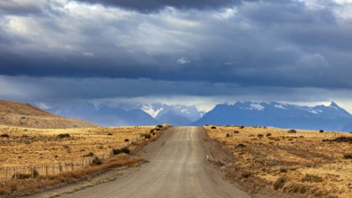 A long gravel road leads to a distant mountain range under a cloudy sky, The Patagonian landscape