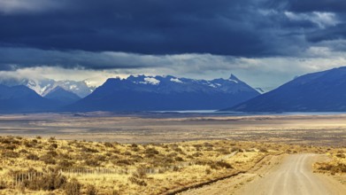 A gravel road leads to a mountain range under a dramatic cloudy sky, The Patagonian landscape near