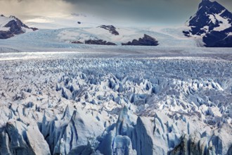 A vast icy landscape stretches out in front of a cloudy sky and majestic mountain peaks, The Perito