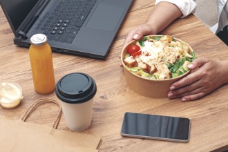 A woman is working on a laptop at home, there is food on the table, salad, coffee and juice,