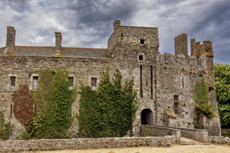 Detailed view of a castle with battlements and ivy under a cloudy sky, Pirou Castle in Normandy,
