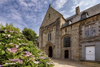 Historic stone church with colourful flowers in the foreground under a blue sky, The Abbey de La