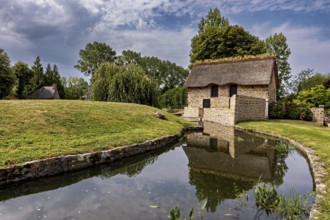 Small house with thatched roof in a quiet, green setting by a stream, The Abbey of La Lucerne in
